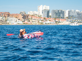 Young girl relaxing safely on a kayak over turquoise Costa Blanca water with a luxury motor boat cruising in the distance.