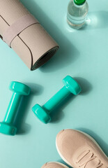 Sport or workout concept flat lay with blue dumbbells, sneakers, yoga mat on the blue teal background. 