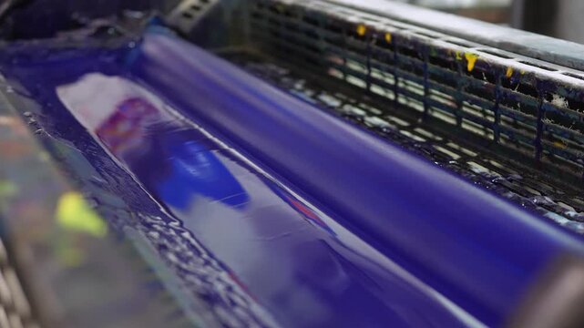 Blue ink rollers inside offset printing press distributing pigment