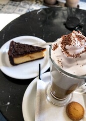 Creamy latte with whipped cream and chocolate shavings served with cheesecake in cozy café setting. A delicious latte topped with whipped cream and chocolate flakes served with a slice of cheesecake