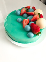 Modern Teal Glazed Cake with Strawberries and Chocolate Spheres. A close-up, high-angle view of a visually stunning round cake covered in a smooth, glossy teal mirror glaze.
