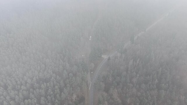Aerial view of a winding road slicing through a dense forest, shrouded in a blanket of mist, creating a monochromatic landscape, Orschwiller, Grand Est, France.