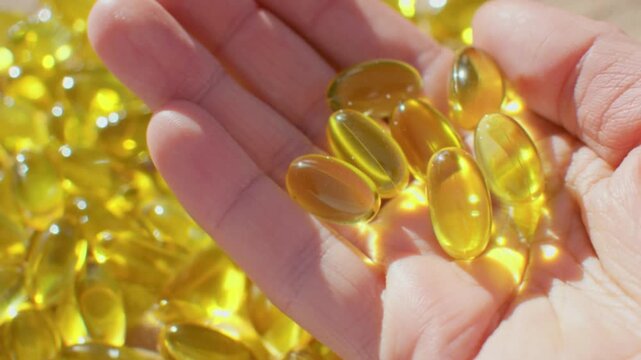 Close up view of hand holding shiny golden softgel capsules in bright sunlight showing health supplement concept with omega oil vitamins and nutritional medicine theme creating wellness lifestyle imag