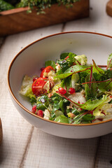 Fresh green salad with mixed vegetables, herbs and light dressing served in a white bowl on rustic table