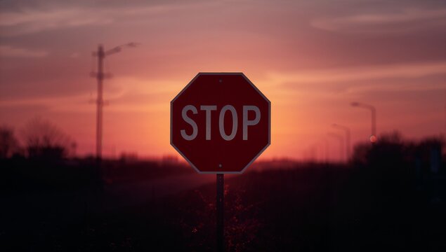 Glowing red octagonal stop sign silhouetting against vivid sunset sky, white letters and metal pole