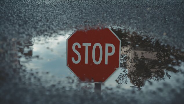 Reflecting red octagonal stop sign floating in puddle on wet roadway, with metal post reflection