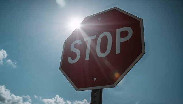Glinting sun flare streaking across red octagon stop sign road showing perforated post bolts clouds - Powered by Adobe
