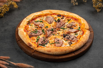 Duck pizza topped with tender sliced meat, cheese and herbs on a rustic wooden board