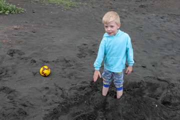 Little blond kid play football and have fun on black sand beach in Kobuleti, Georgia