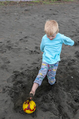 Little blond kid play football and have fun on black sand beach in Kobuleti, Georgia