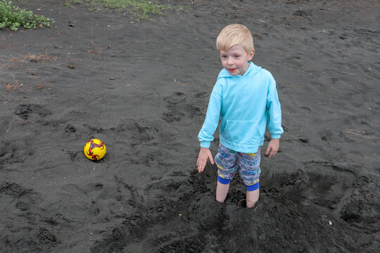 Little blond kid play football and have fun on black sand beach in Kobuleti, Georgia