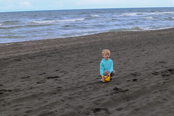 Little blond kid play football and have fun on black sand beach in Kobuleti, Georgia