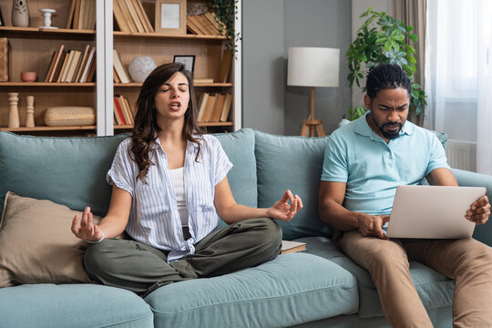 Couple balancing remote life at home, one partner stressed with laptop deadlines while the other meditates to stay centered, illustrating mindful relationship care, mental health, focus and resilience