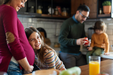 Happy daughter hugging belly her expecting mother at home. Excited girl listening to baby movement