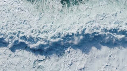 Aerial view from a drone flying through a winter snowstorm as a powerful ocean wave crashes over snow-covered volcanic cliffs. Stormy winter surf batters the rugged Icelandic coast - Powered by Adobe