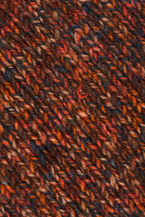 A full-frame, close-up texture of dark brown knit fabric with a speckled, heathered pattern created by mixed yarn threads in shades of red, orange, and blue