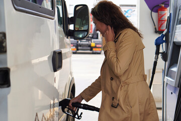 A middle-aged woman with curly hair, filling up the tank of her camper van at a gas station. © Inspiraciones