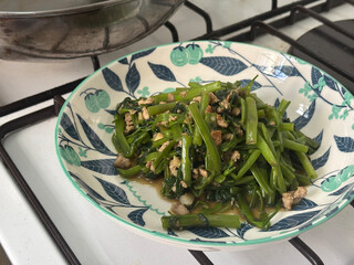 A vibrant dish of stir-fried morning glory, featuring tender greens and minced meat in a glossy oyster sauce. Served in a decorative bowl, this appetizing meal showcases fresh ingredients.