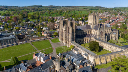 Aerial view of the magnificent Wells Cathedral standing tall amidst the green Cathedral Green, its stonework bathed in sunlight, Wells, England, United Kingdom.