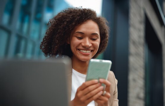 black woman checking smartphone laughing, casual blazer, focused expression, reading message thread, natural