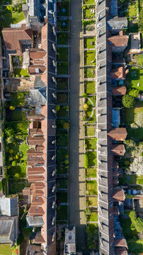 Aerial view of the historic Vicar's Close reveals symmetrical rows of aged stone buildings, casting long shadows across manicured lawns in a serene tableau, Wells, England, United Kingdom.