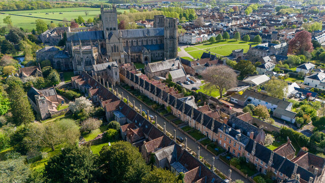 Aerial view of the ancient Vicar's Close stretching towards the majestic Wells Cathedral, a symphony of aged stone against the lush English landscape, Wells, England, United Kingdom.