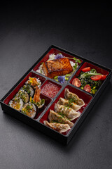 Bento box with gyoza, sushi, salmon and tempura on dark background isolated for menu