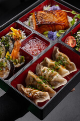Bento box with gyoza, sushi, salmon and tempura on dark background isolated for menu