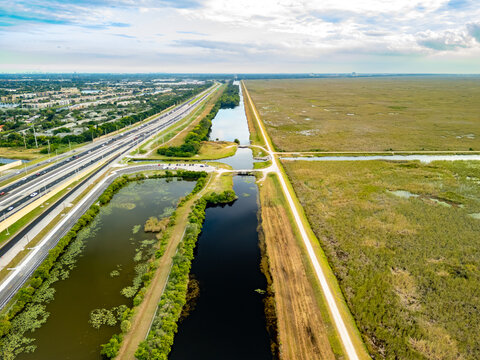 Aerial view of a stark contrast between urban development and raw nature, divided by canals and roadways, Coral Springs, Florida, United States.