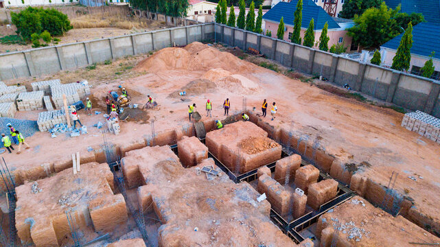 Aerial view of construction workers busy on a construction site with foundation trenches, surrounded by walls and buildings, Katsina, Katsina, Nigeria.