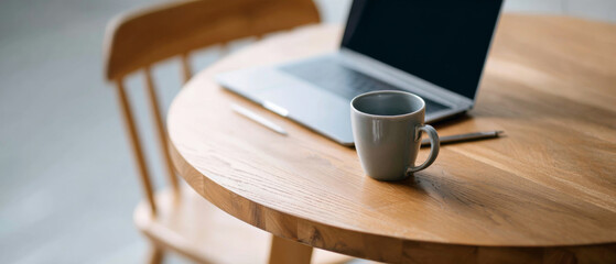 Wooden round table with ceramic coffee mug and open laptop in cozy home setting with natural light
