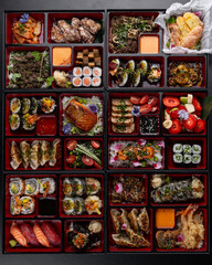Huge bento box with Japanese cuisine dishes - sushi, sashimi, gyoza, tempura and more on a dark background isolated