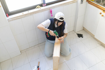 Young woman assembling wooden furniture using electric drill