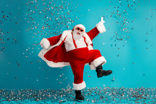 Santa in red suit with hat beard and belt dancing with confetti against blue background for holiday celebration and festive promotion