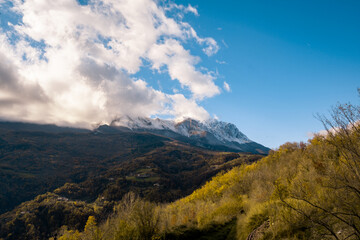 Snow capped mountain peaks emerging from clouds, an autumn landscape with colorful hillsides and clear blue sky, Gran Sasso, Abruzzo, Italy