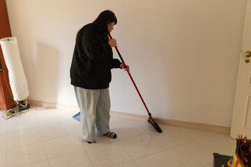 Woman sweeping tiled floor with broom and dustpan