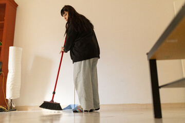 Young woman sweeping floor doing daily household chores
