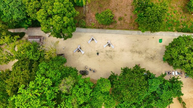 Aerial view of a sandy playground nestled between lush green trees casting shadows, a tranquil escape from the city's hustle, Ko Kaeo, Phuket, Thailand.