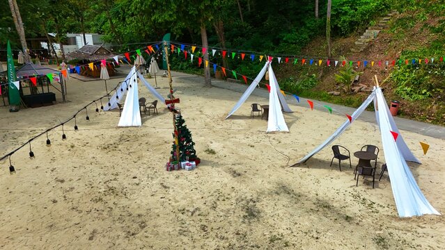 Aerial view of the sandy beach adorned with festive decorations, including colorful flags and tents, creating a vibrant contrast against the natural backdrop, Ko Kaeo, Phuket, Thailand.