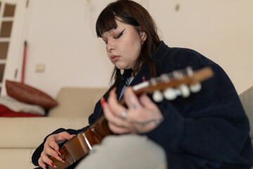 Young woman playing acoustic guitar at home, creating music