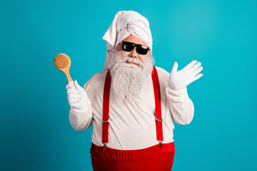 Santa Claus in a white outfit with red suspenders and a towel on his head poses with wooden scrub brush against a blue background