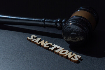 A wooden gavel next to the word SANCTIONS on a dark background. International law, legal penalties, trade restrictions, economic policy, and corporate punishment concept.