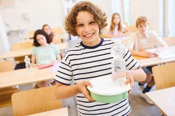 Smiling student holding lunch tray and bottle in classroom setting