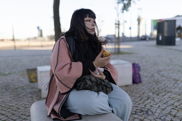 Young person eating an apple on urban bench