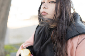 Young woman eating apple outdoors feeling pensive
