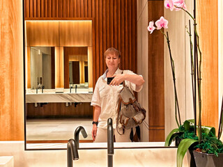 Woman taking a selfie in a modern restroom with wooden accents and an orchid plant