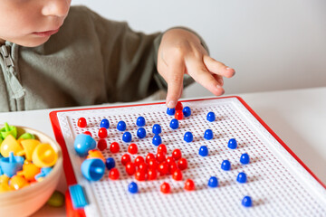 Child placing colored pegs on mosaic board. Image symbolizes learning process, creativity development, motor skill training, and focus in early childhood.