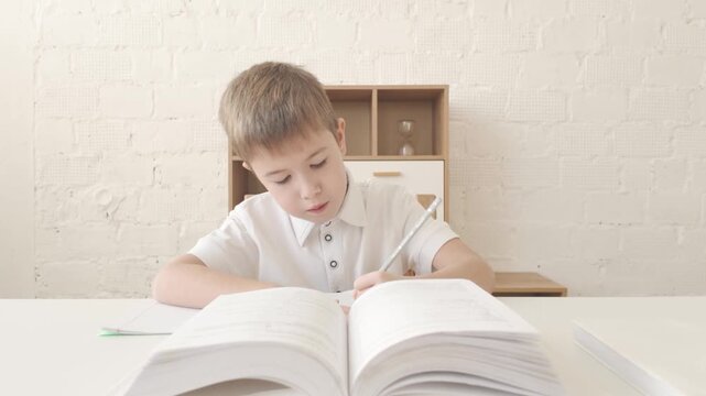 Boy writes homework in copybook using textbook on the table. 4K video for school lessons or education themes