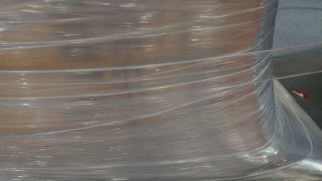 Stretch film is tightly wrapped around a pallet of boxes in a warehouse setting, efficient packaging and secure storage. The clear film encases the items, ensuring stability during transit.