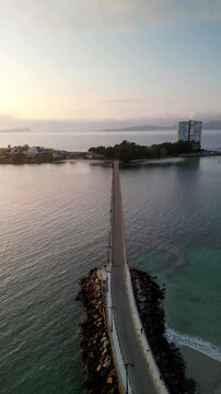 Aerial view of a modern bridge leading to Toralla island with a tall building, reflecting soft light on the water, illa de Toralla, Pontevedra, Spain.